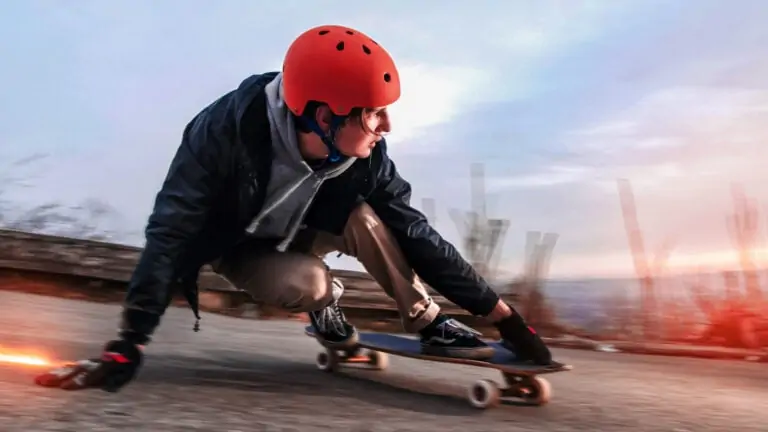 Young man with safety gear and helmet riding down a hill on a skateboard